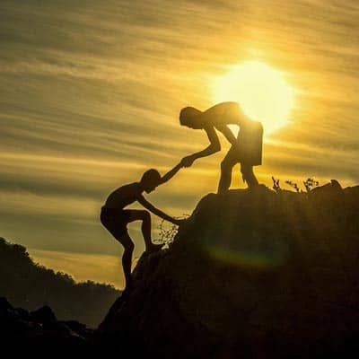  A person helping another to climb a mountain.