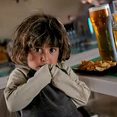 A young girl sitting beside a glass of beer.