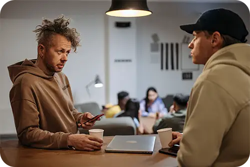 Two men talking on the edge of a table.